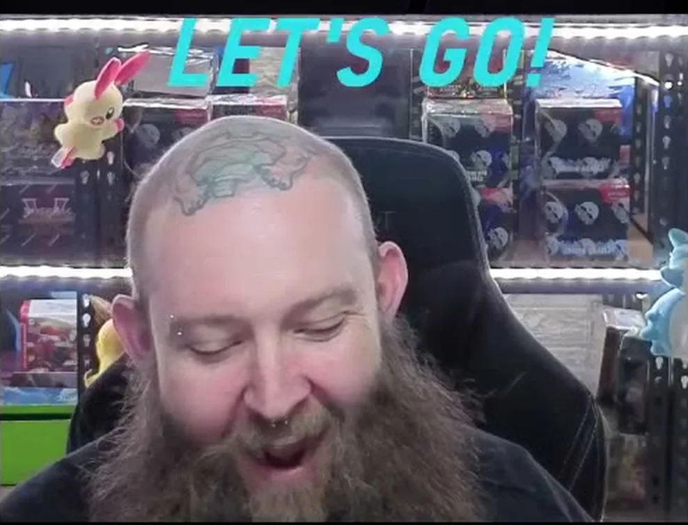 Josh laughing mid-show at his desk, shelves of sealed product and graded cards behind him.